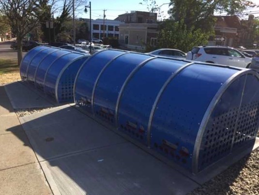 The image displays two domed blue bike lockers located at the Milford train station.